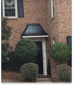 front of a brick home with trees and shrubs surrounding entryway black doors