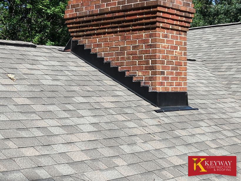 New black step flashing where a brick chimney meets the roof in Charlotte, NC
