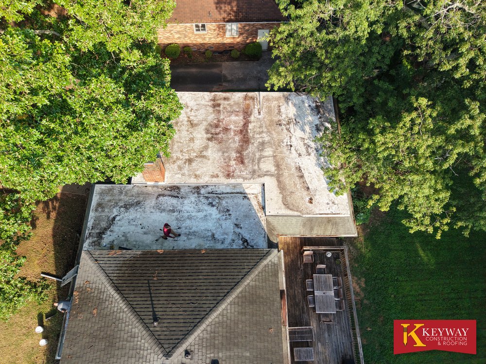 Drone view of a Charlotte NC roof with a large flat section and chimney before work began