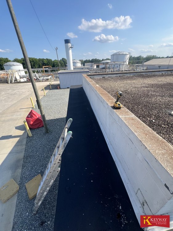 Commercial parapet wall wrapped in new white membrane with new dark membrane at its base