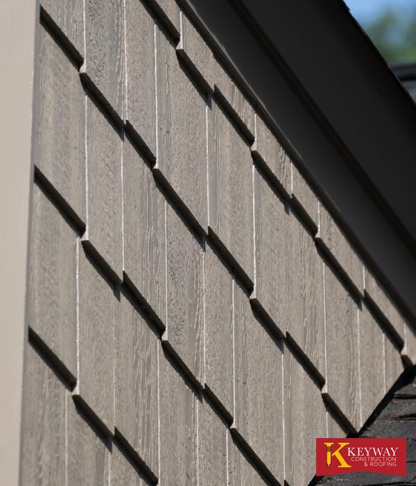 Close up of new shake style siding courses and metal trim on a repaired dormer cheek wall where it meets the shingled roof