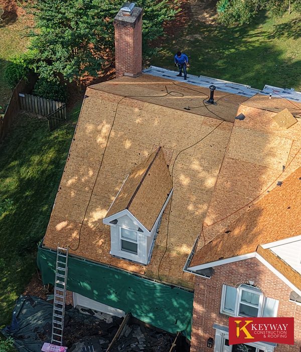 Matthews NC brick home stripped to bare roof decking during a full tear off, with a Keyway roofer working near the chimney